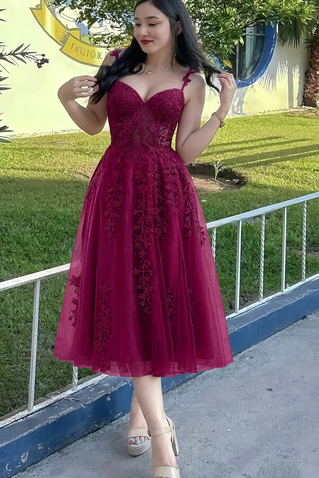 Front view of the LVLVS Adeline burgundy midi dress outdoors beside a railing, showing the lace bodice and flared skirt.