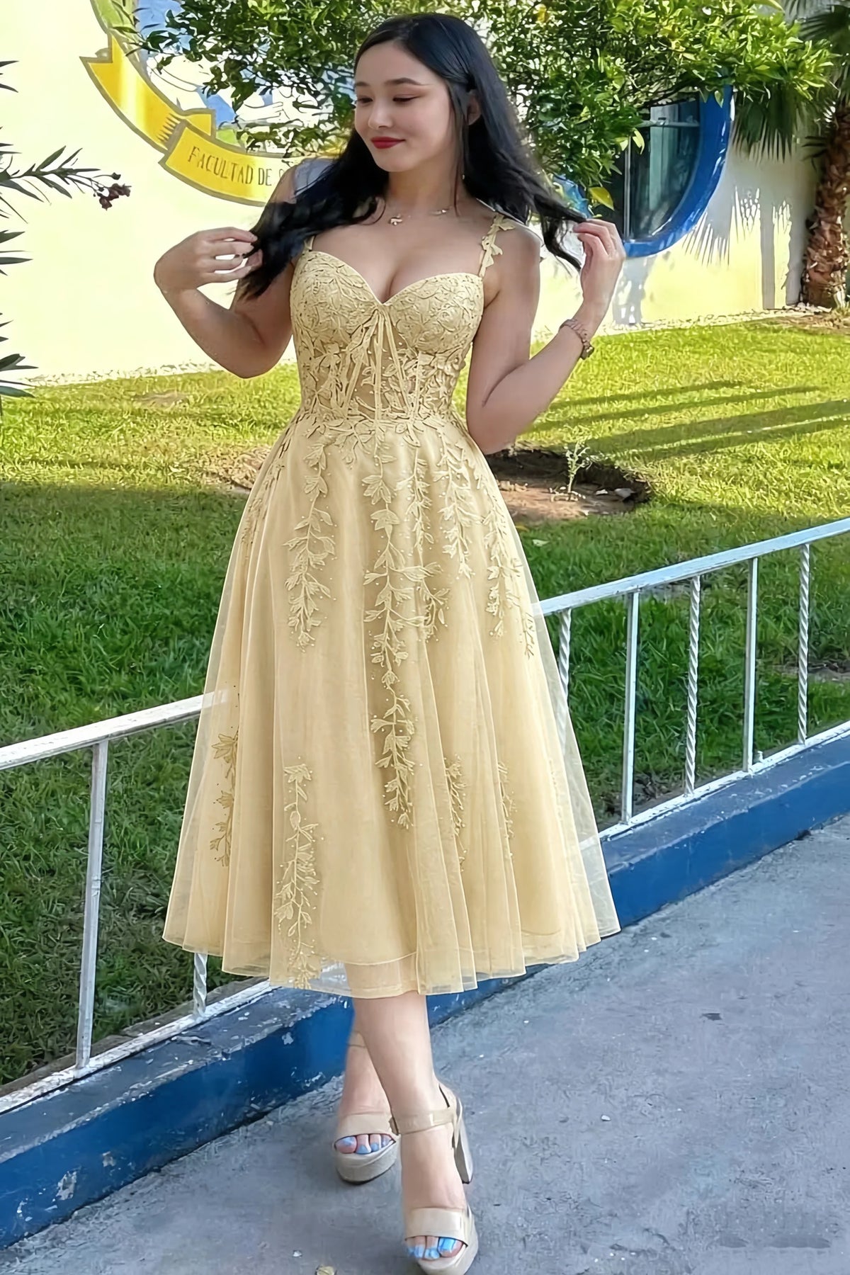 Front view of the LVLVS Adeline champagne midi dress outdoors beside a railing, showing the lace bodice and flared skirt.
