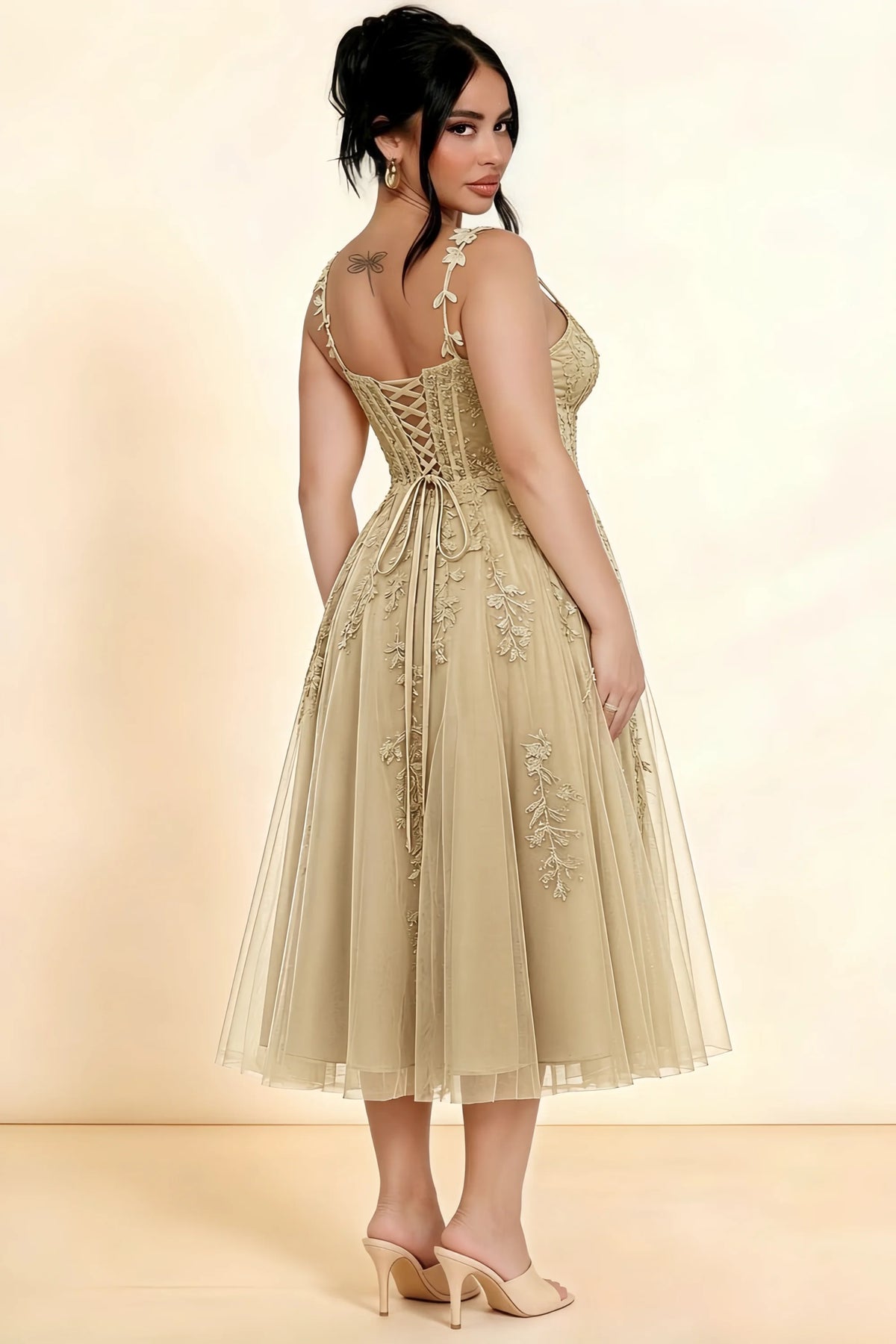 Rear three-quarter view of a model wearing the LVLVS Adeline champagne midi dress, showing the lace-up back and layered midi skirt.