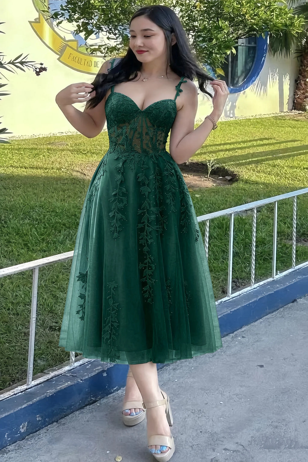 Front view of the LVLVS Adeline dark green midi dress outdoors beside a railing, showing the lace bodice and flared skirt.