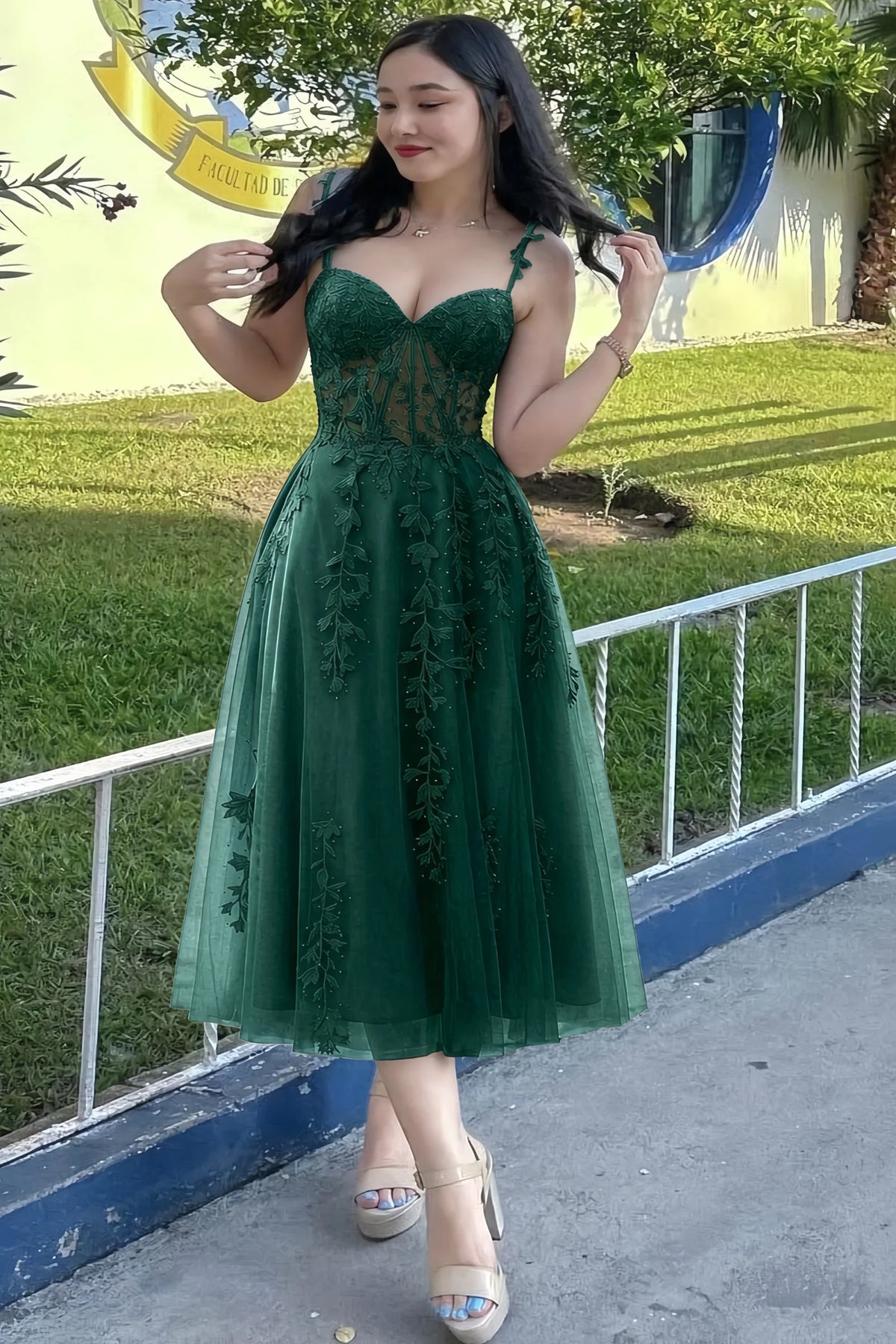 Front view of the LVLVS Adeline dark green midi dress outdoors beside a railing, showing the lace bodice and flared skirt.