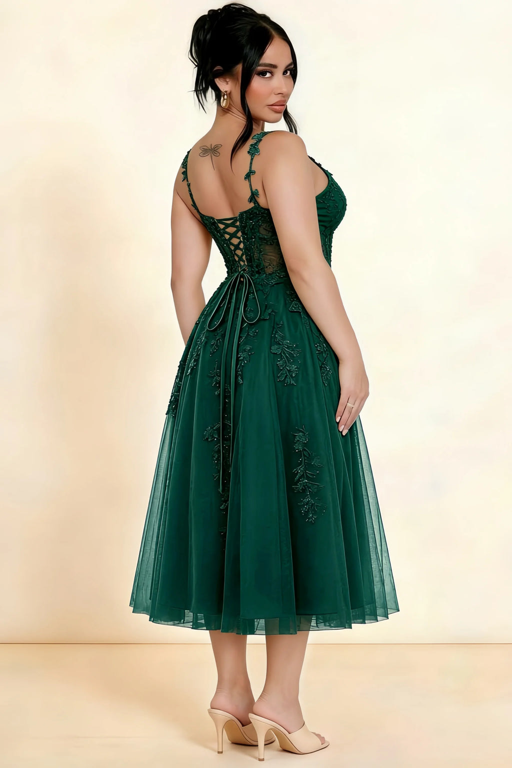 Rear three-quarter view of a model wearing the LVLVS Adeline dark green midi dress, showing the lace-up back and layered midi skirt.