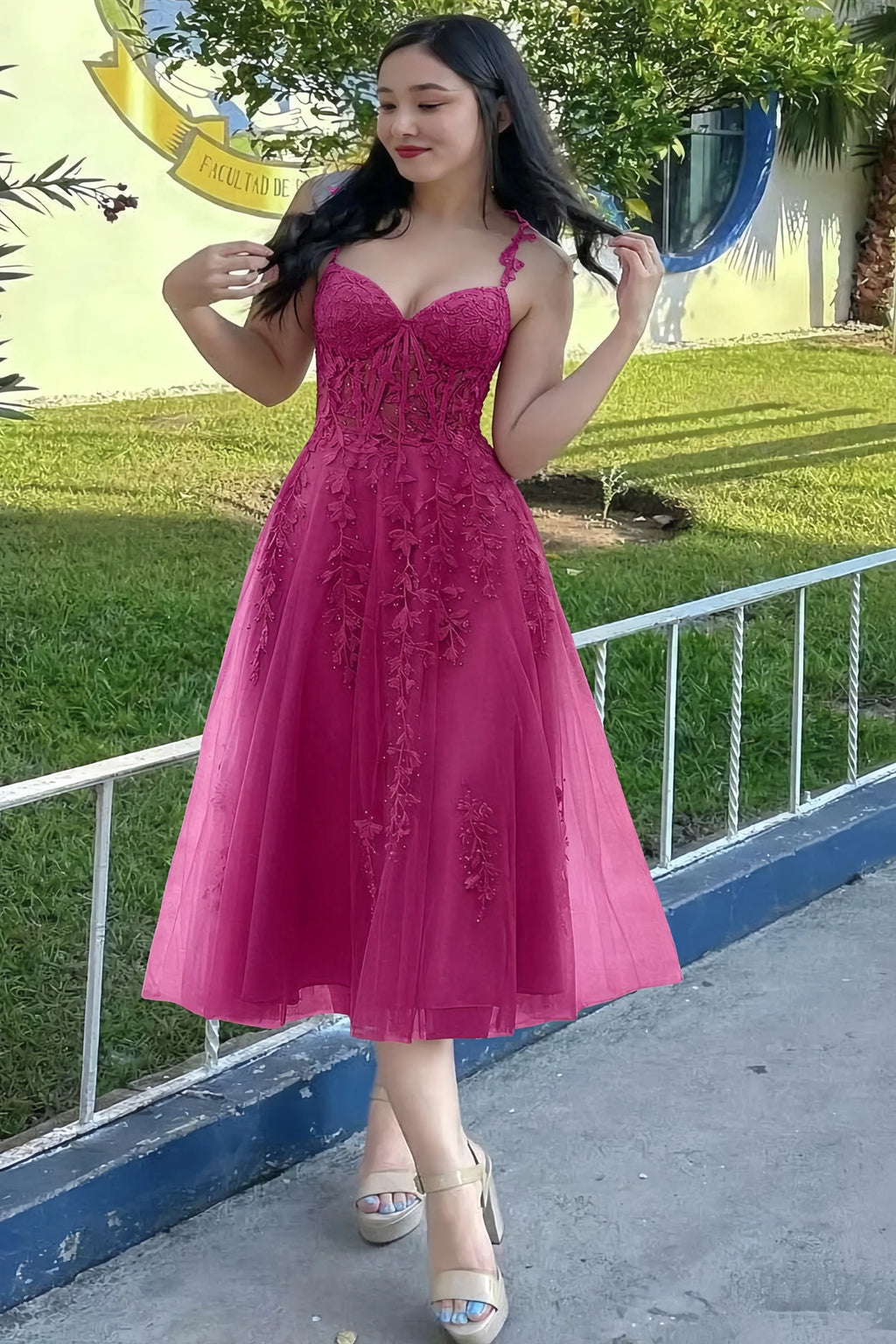 Front view of the LVLVS Adeline fuchsia midi dress outdoors beside a railing, showing the lace bodice and flared skirt.