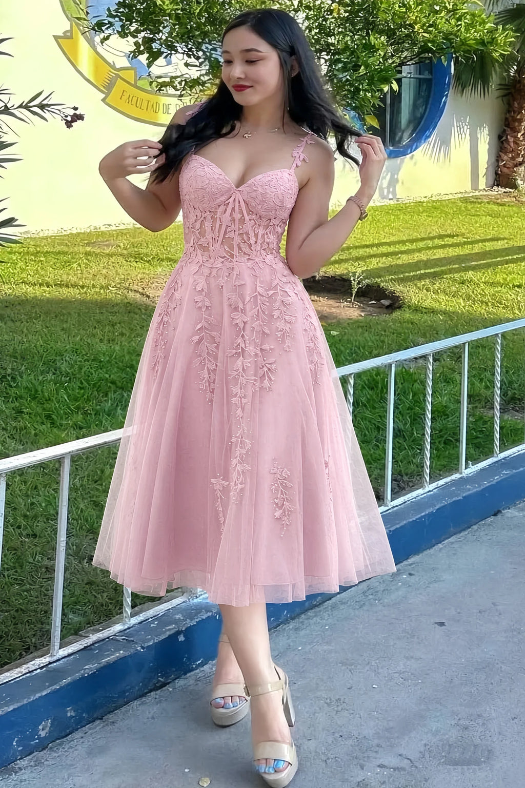 Front view of the LVLVS Adeline light pink midi dress outdoors beside a railing, showing the lace bodice and flared skirt.