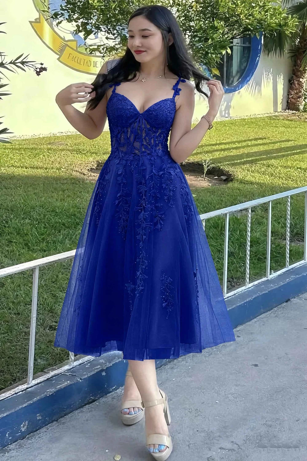 Front view of the LVLVS Adeline royal blue midi dress outdoors beside a railing, showing the lace bodice and flared skirt.