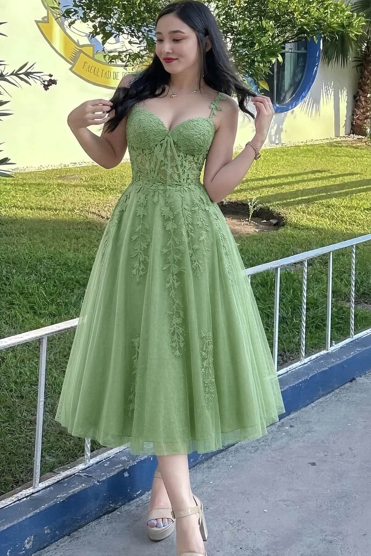 Front view of the LVLVS Adeline sage green midi dress outdoors beside a railing, showing the lace bodice and flared skirt.