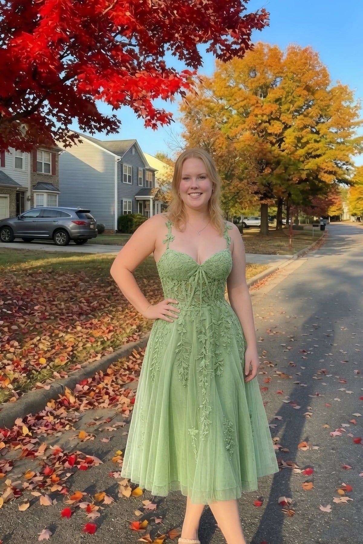 Front view of the LVLVS Adeline sage green midi dress on an autumn street, with red and yellow leaves in the background.