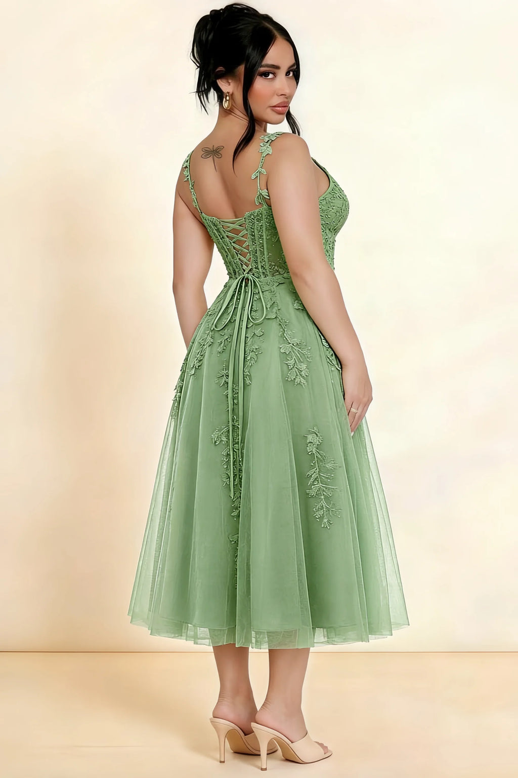Rear three-quarter view of a model wearing the LVLVS Adeline sage green midi dress, showing the lace-up back and layered midi skirt.