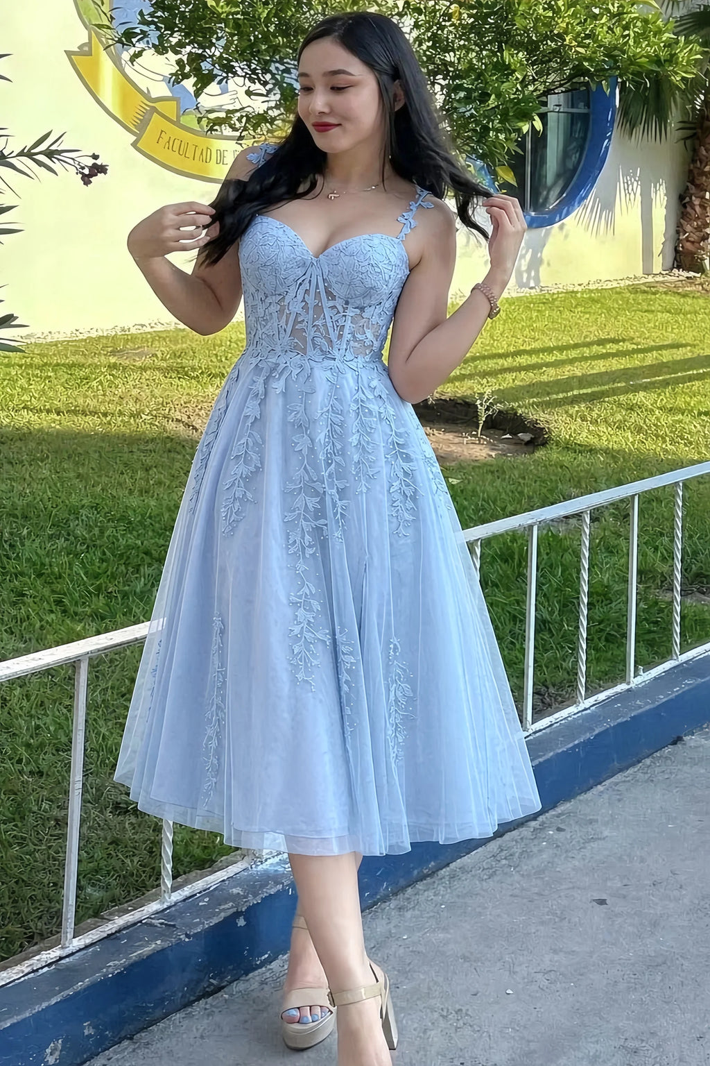 Front view of the LVLVS Adeline sky blue midi dress outdoors beside a railing, showing the lace bodice and flared skirt.