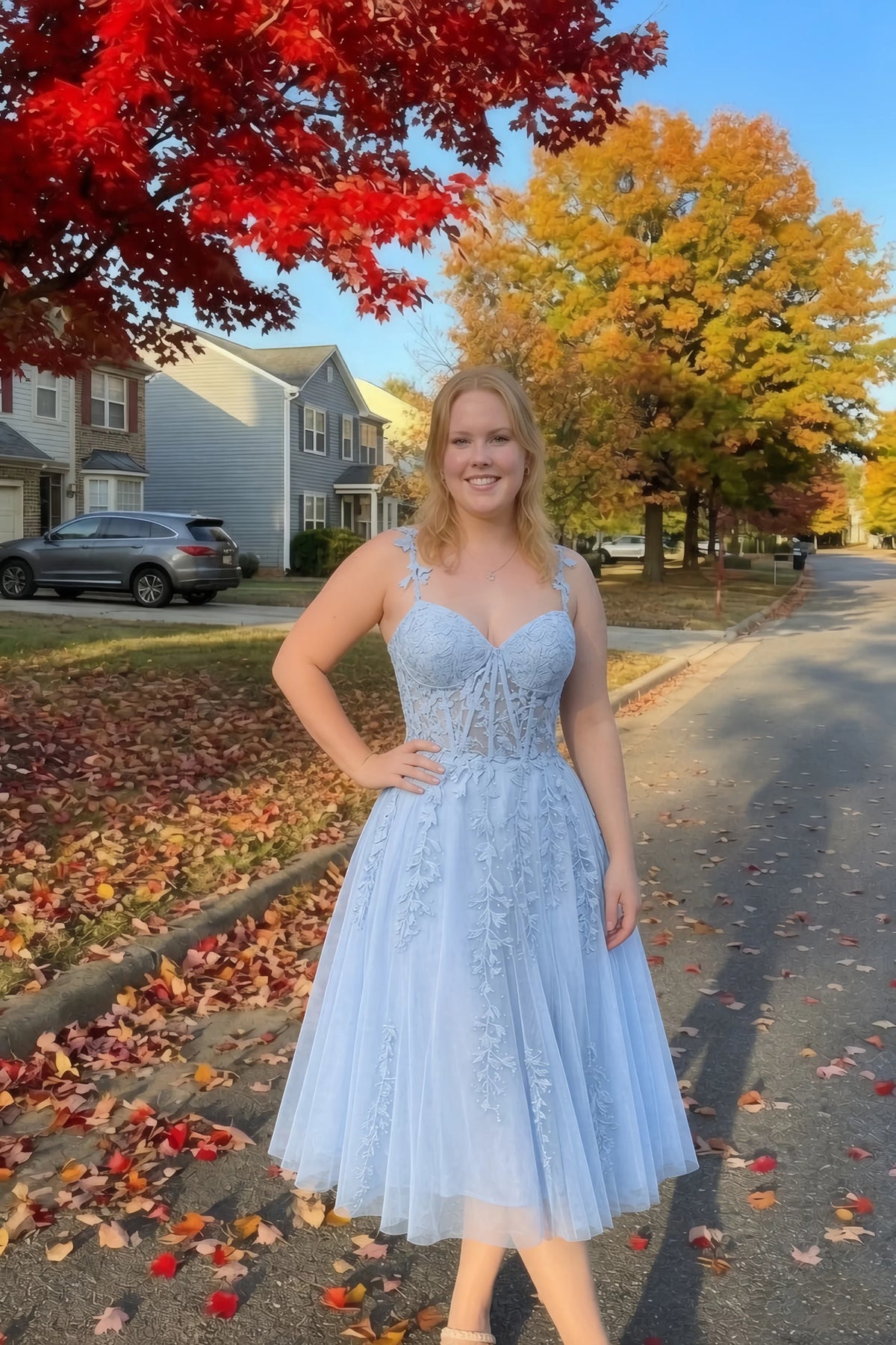 Front view of the LVLVS Adeline sky blue midi dress on an autumn street, with red and yellow leaves in the background.