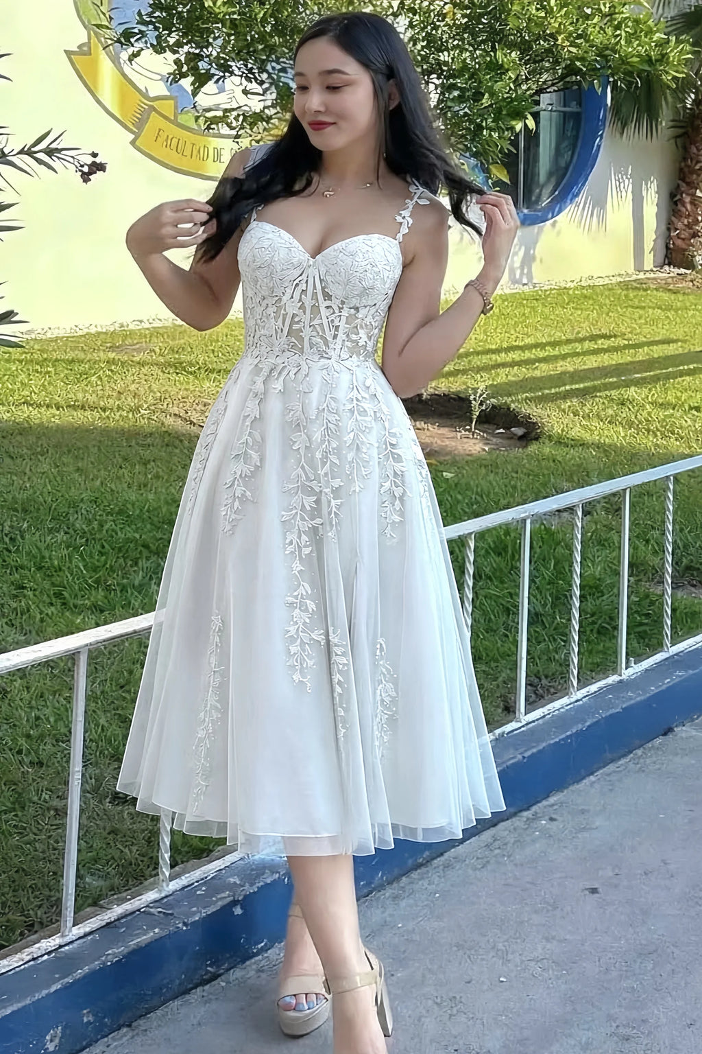 Front view of the LVLVS Adeline white midi dress outdoors beside a railing, showing the lace bodice and flared skirt.