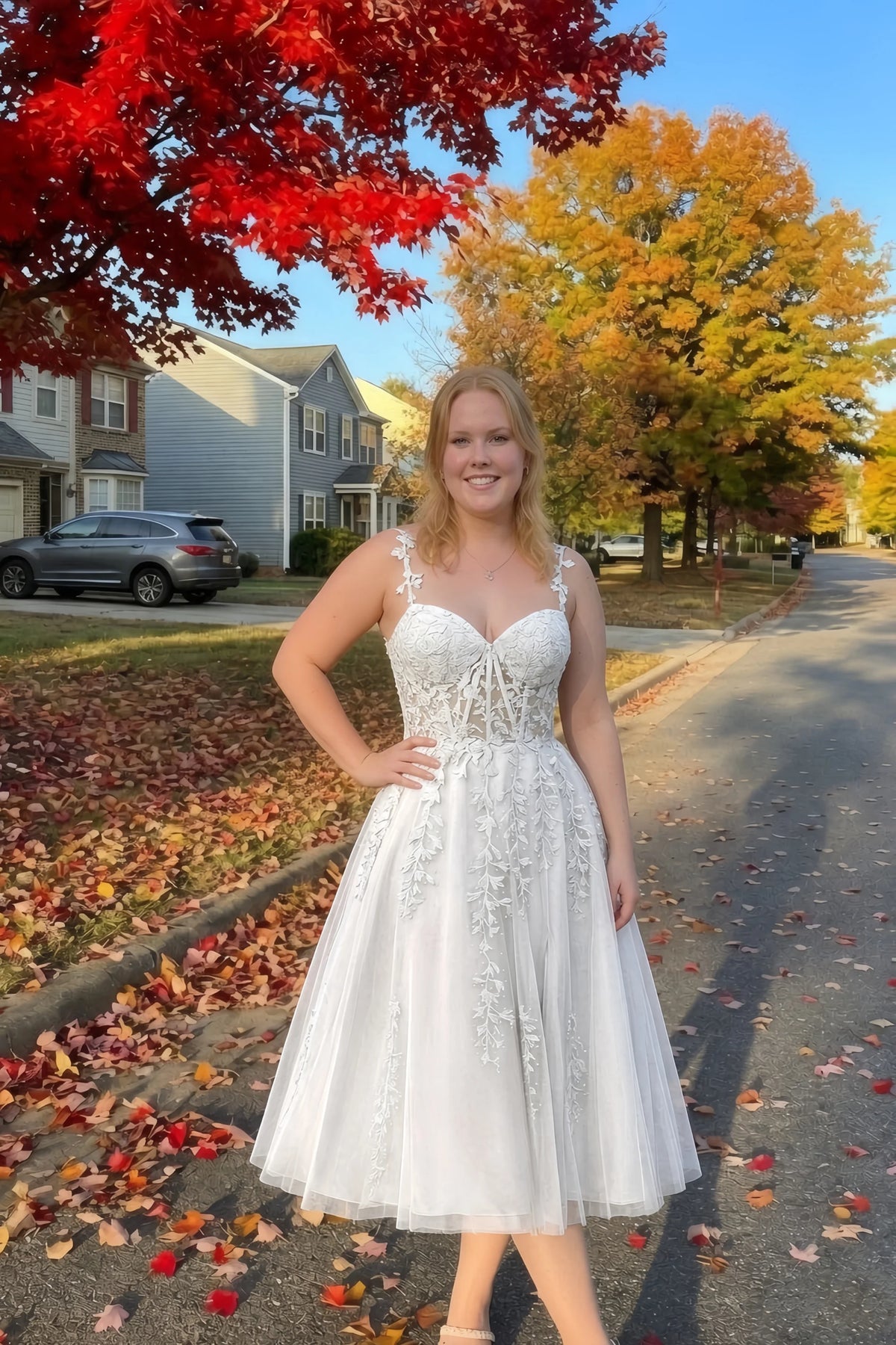 Front view of the LVLVS Adeline white midi dress on an autumn street, with red and yellow leaves in the background.