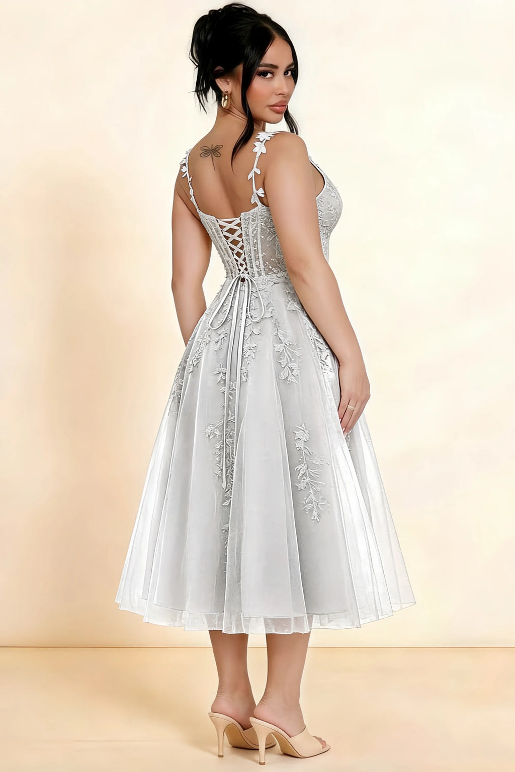 Rear three-quarter view of a model wearing the LVLVS Adeline white midi dress, showing the lace-up back and layered midi skirt.