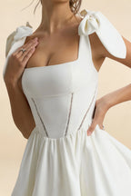Detailed close up of LVLVS Cassandra white dress bodice, highlighting the structured square neckline, fabric texture of stretch crepe, and delicate bow embellishment