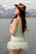 Real customer wearing Christine mint green sequin dress with feather details by the lake, stylish travel and event wear.