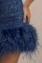 Detailed macro shot of Christine navy dress feather trim and sequin texture, close-up of the fluffy feathers and shiny fabric material for luxury party wear.