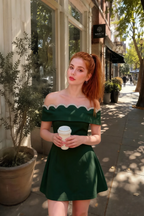 Customer wearing Christy dark green crepe cocktail dress for bridesmaid party, stylish off-the-shoulder summer look on the street.