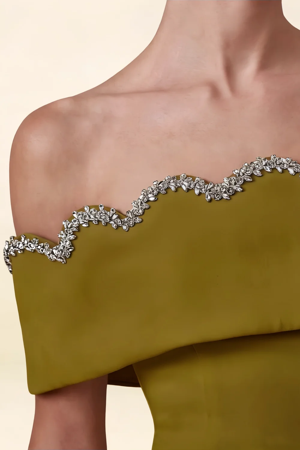 Macro close-up of olive crepe fabric and sparkling rhinestone off-shoulder neckline trim.