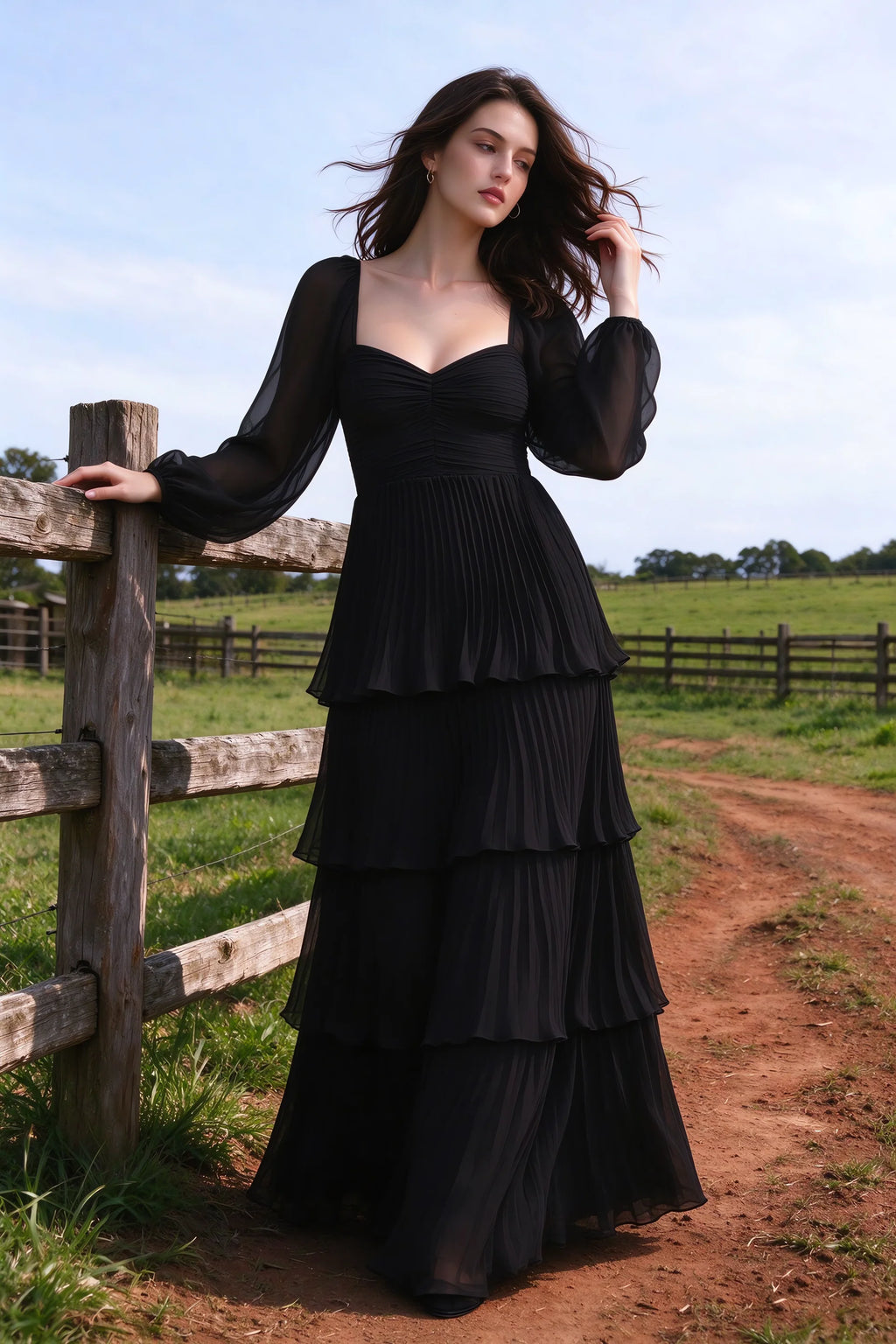 Outdoor front view by a countryside fence of Sienna black tiered pleated maxi dress with a long flowing skirt