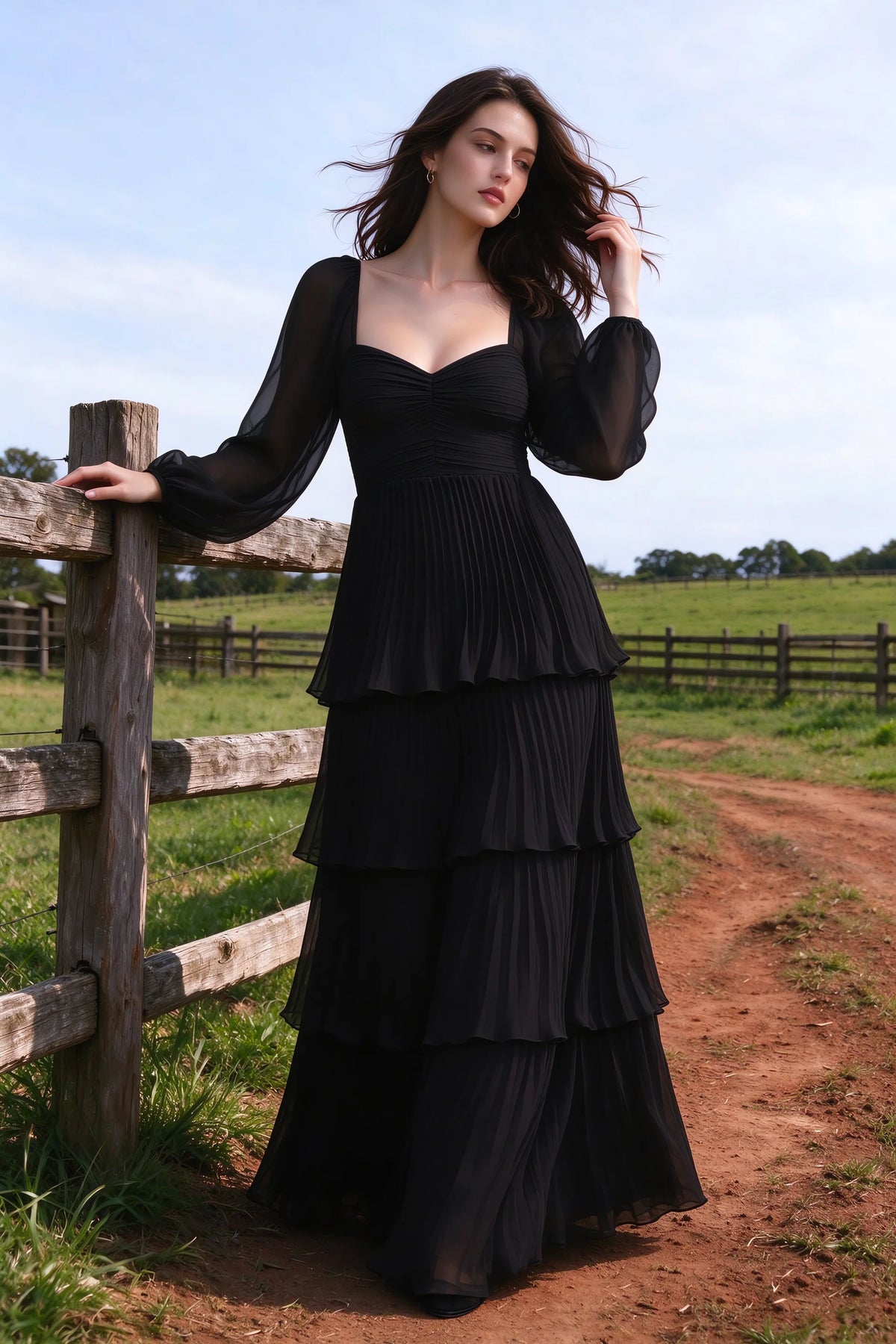 Outdoor front view by a countryside fence of Sienna black tiered pleated maxi dress with a long flowing skirt