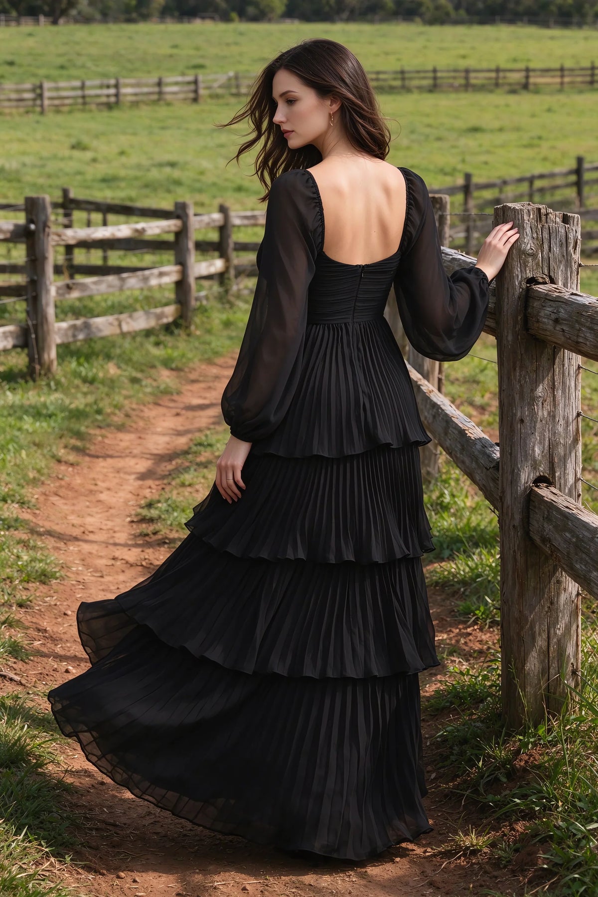 Outdoor rear view by a countryside fence of Sienna black tiered pleated maxi dress with a long flowing skirt