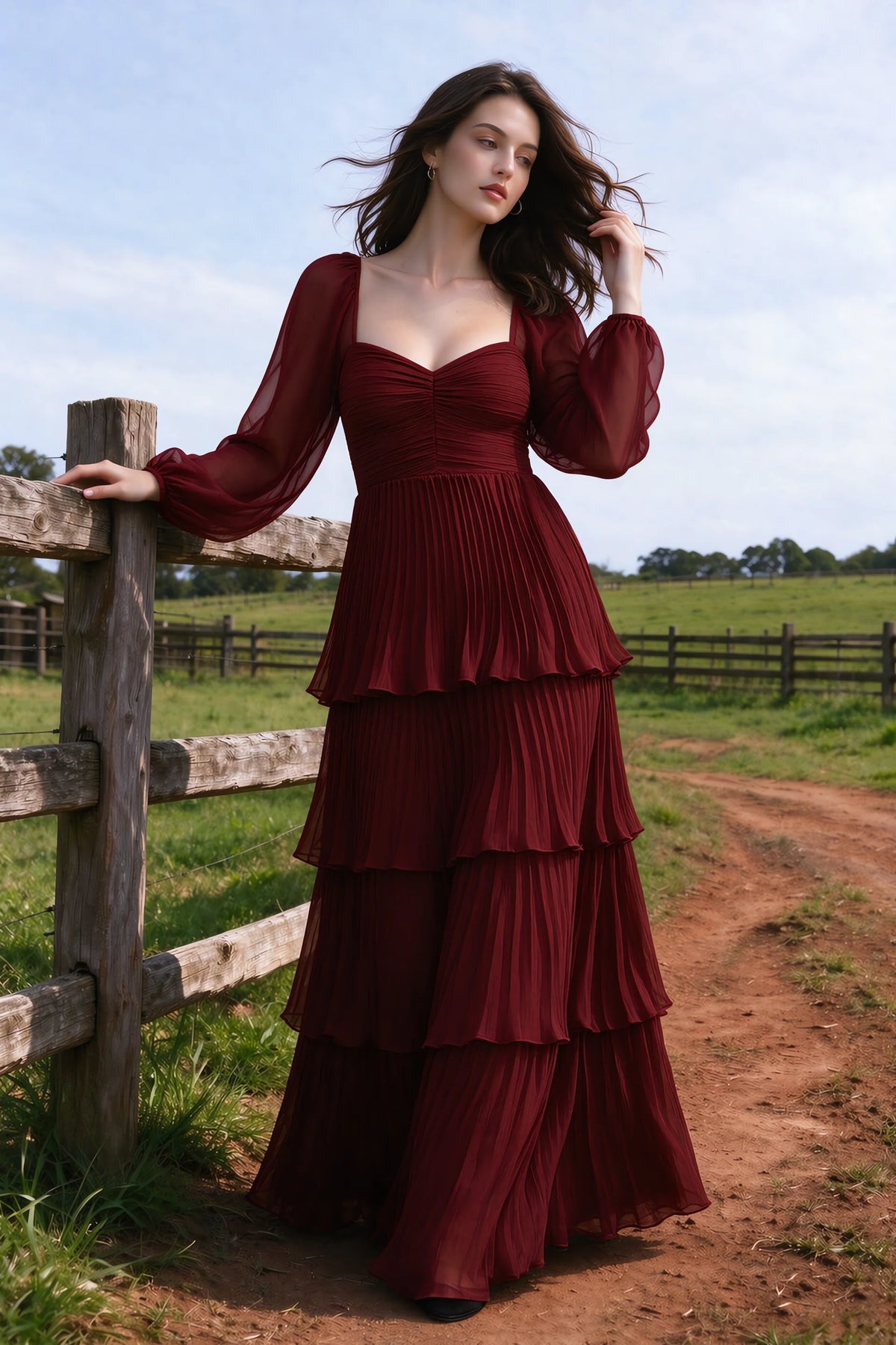 Outdoor front view by a countryside fence of Sienna burgundy tiered pleated maxi dress with a long flowing skirt