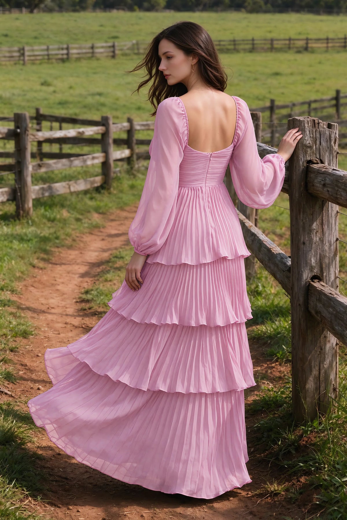 Outdoor rear view by a countryside fence of Sienna candy pink tiered pleated maxi dress with a long flowing skirt