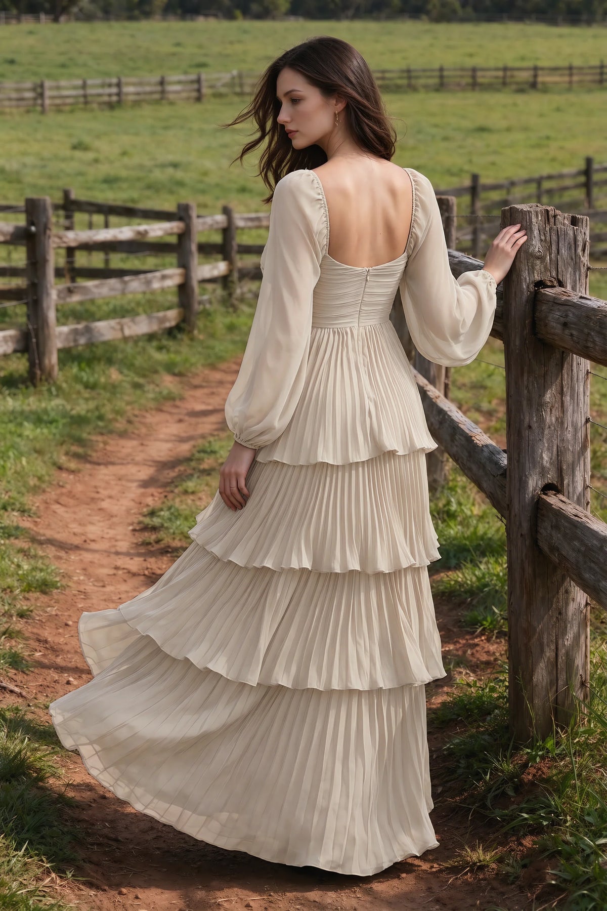 Outdoor rear view by a countryside fence of Sienna cream tiered pleated maxi dress with a long flowing skirt