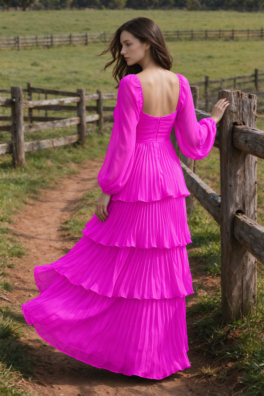 Outdoor rear view by a countryside fence of Sienna fuchsia tiered pleated maxi dress with a long flowing skirt