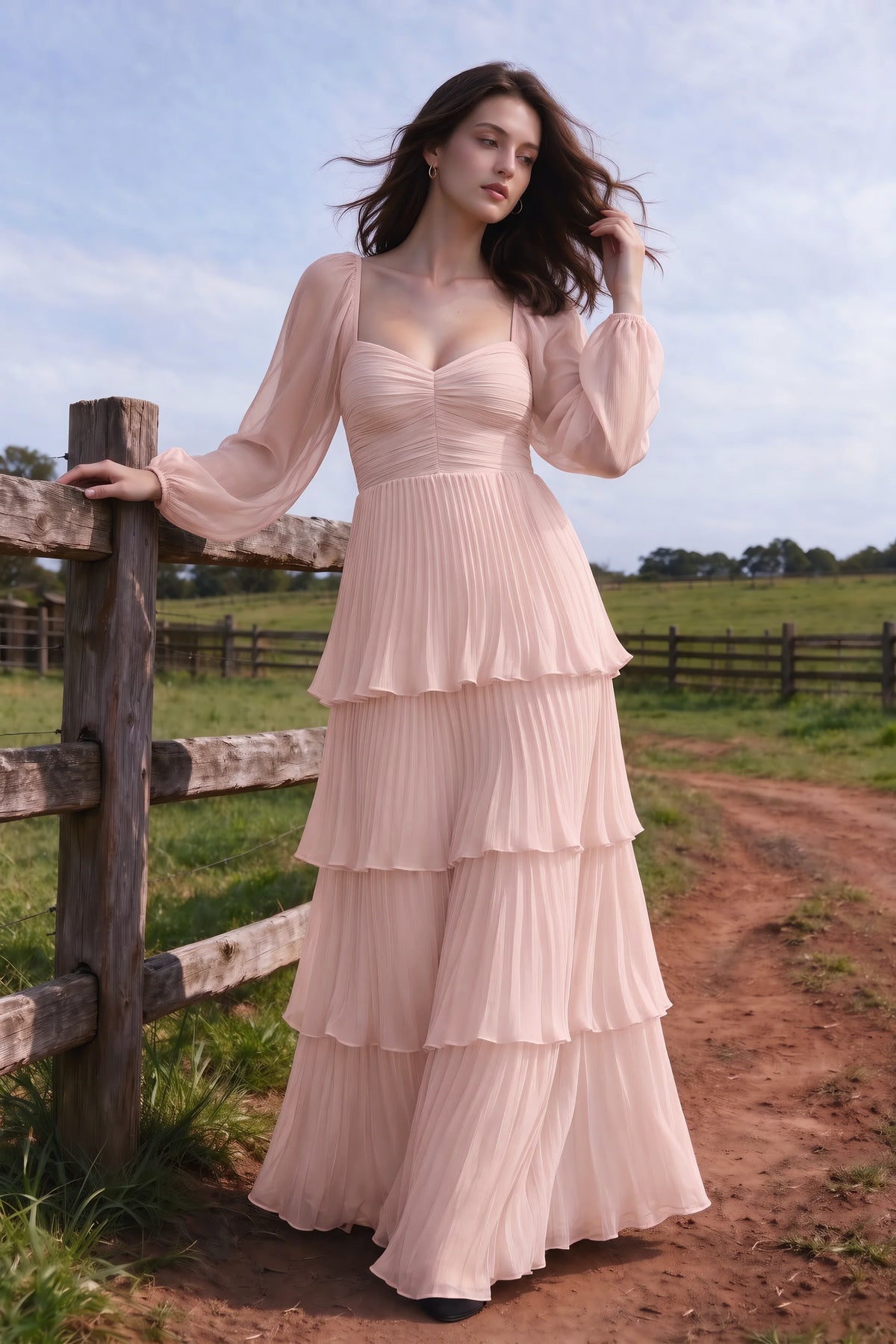Outdoor front view by a countryside fence of Sienna haze pink tiered pleated maxi dress with a long flowing skirt