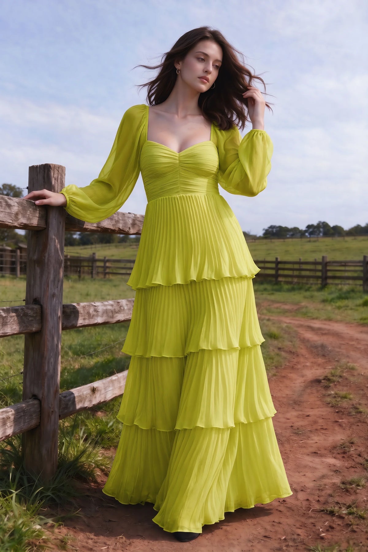 Outdoor front view by a countryside fence of Sienna lemon green tiered pleated maxi dress with a long flowing skirt