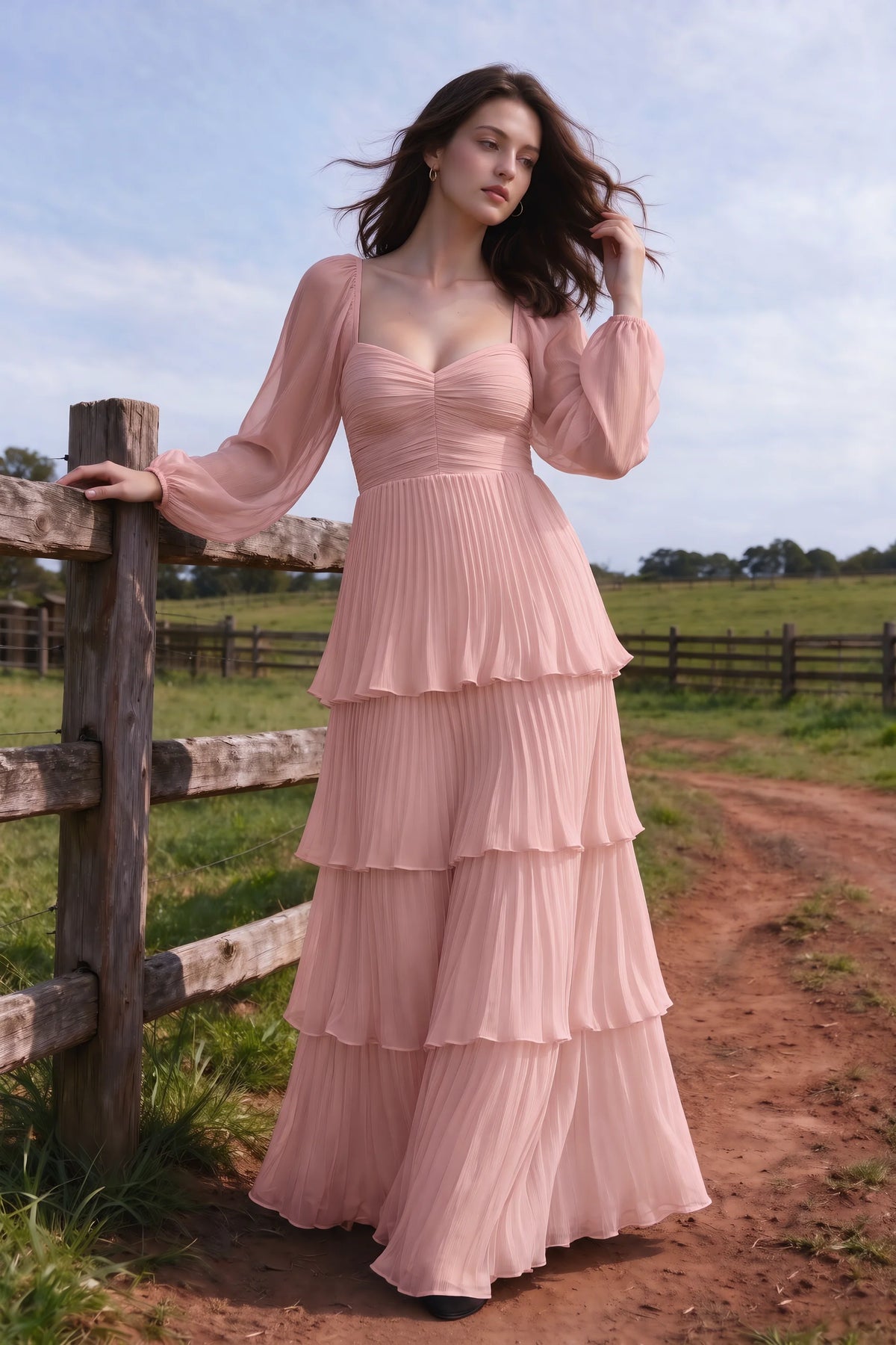 Outdoor front view by a countryside fence of Sienna light pink tiered pleated maxi dress with a long flowing skirt