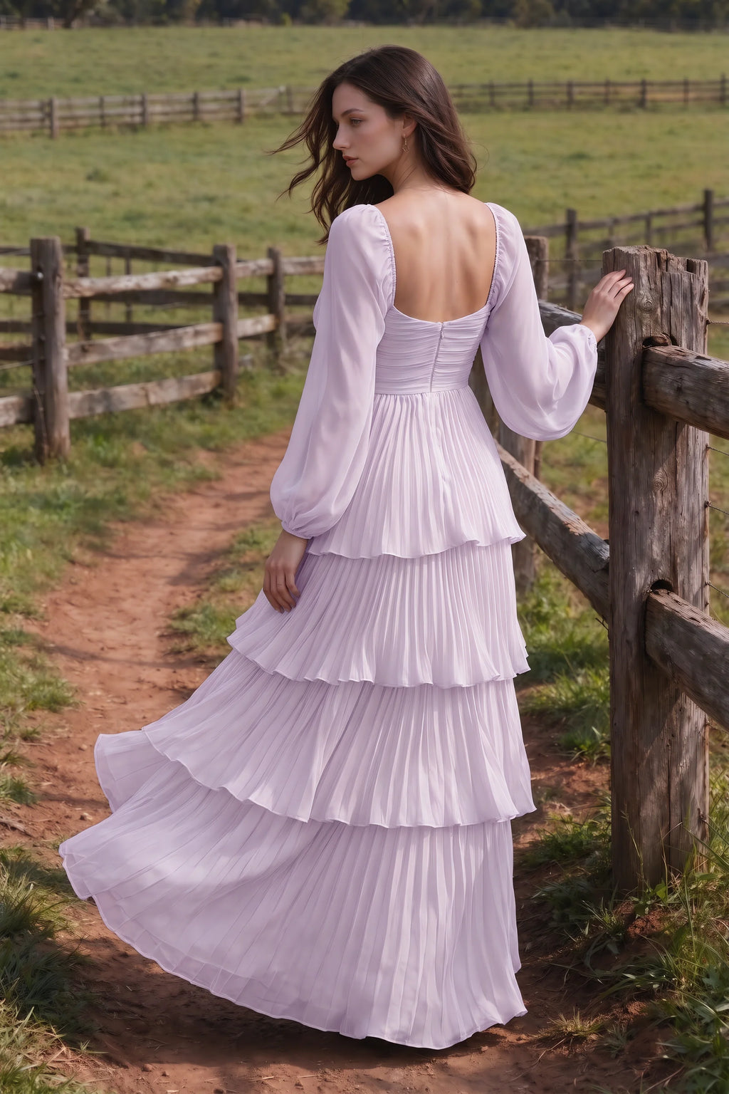 Outdoor rear view by a countryside fence of Sienna lilac tiered pleated maxi dress with a long flowing skirt
