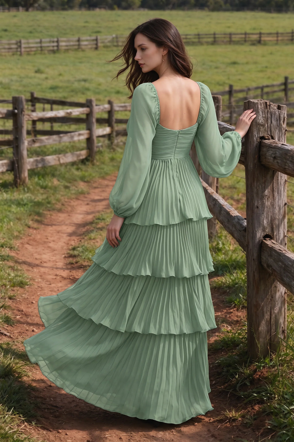 Outdoor rear view by a countryside fence of Sienna matcha green tiered pleated maxi dress with a long flowing skirt