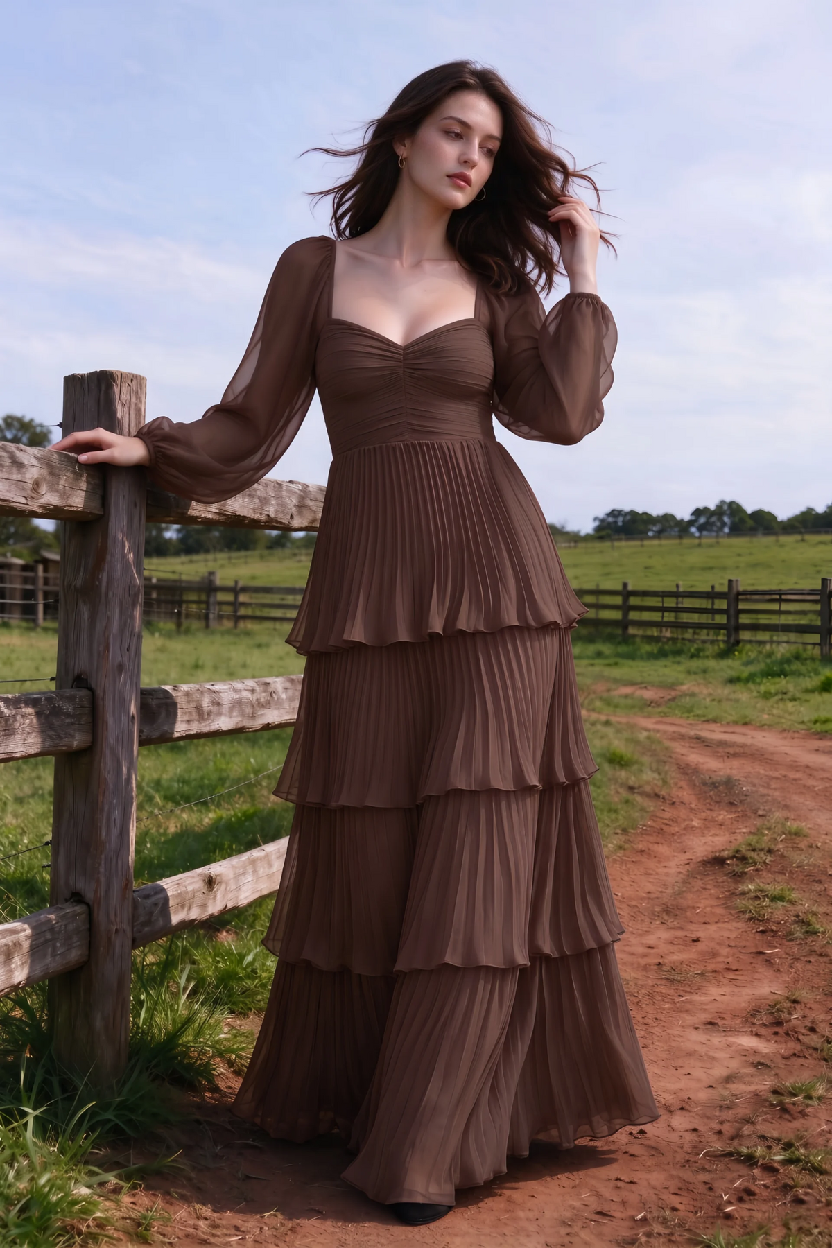 Outdoor front view by a countryside fence of Sienna mocha tiered pleated maxi dress with a long flowing skirt