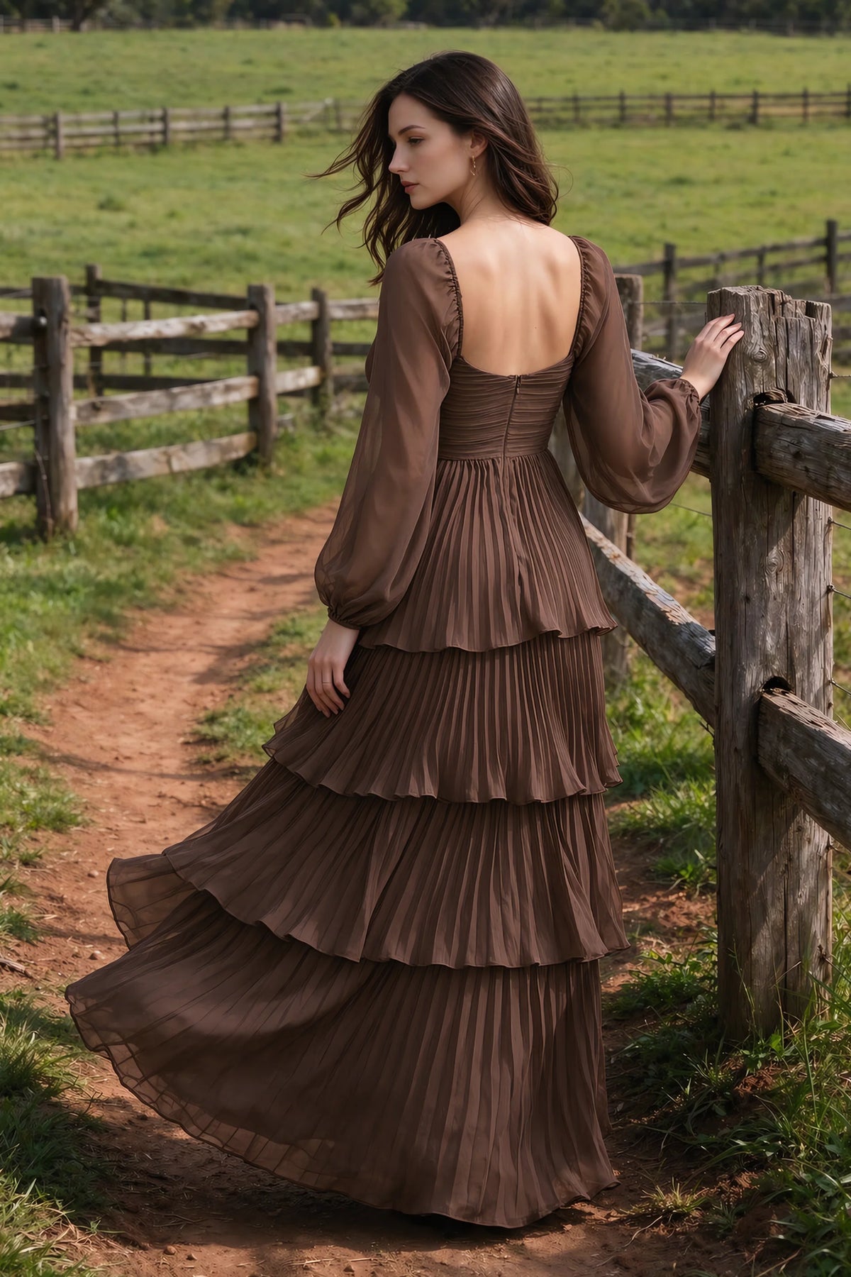 Outdoor rear view by a countryside fence of Sienna mocha tiered pleated maxi dress with a long flowing skirt