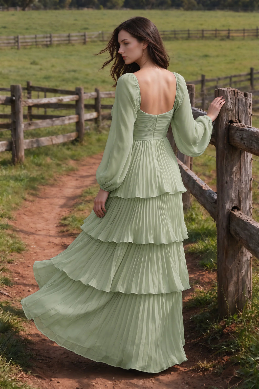 Outdoor rear view by a countryside fence of Sienna pistachio tiered pleated maxi dress with a long flowing skirt