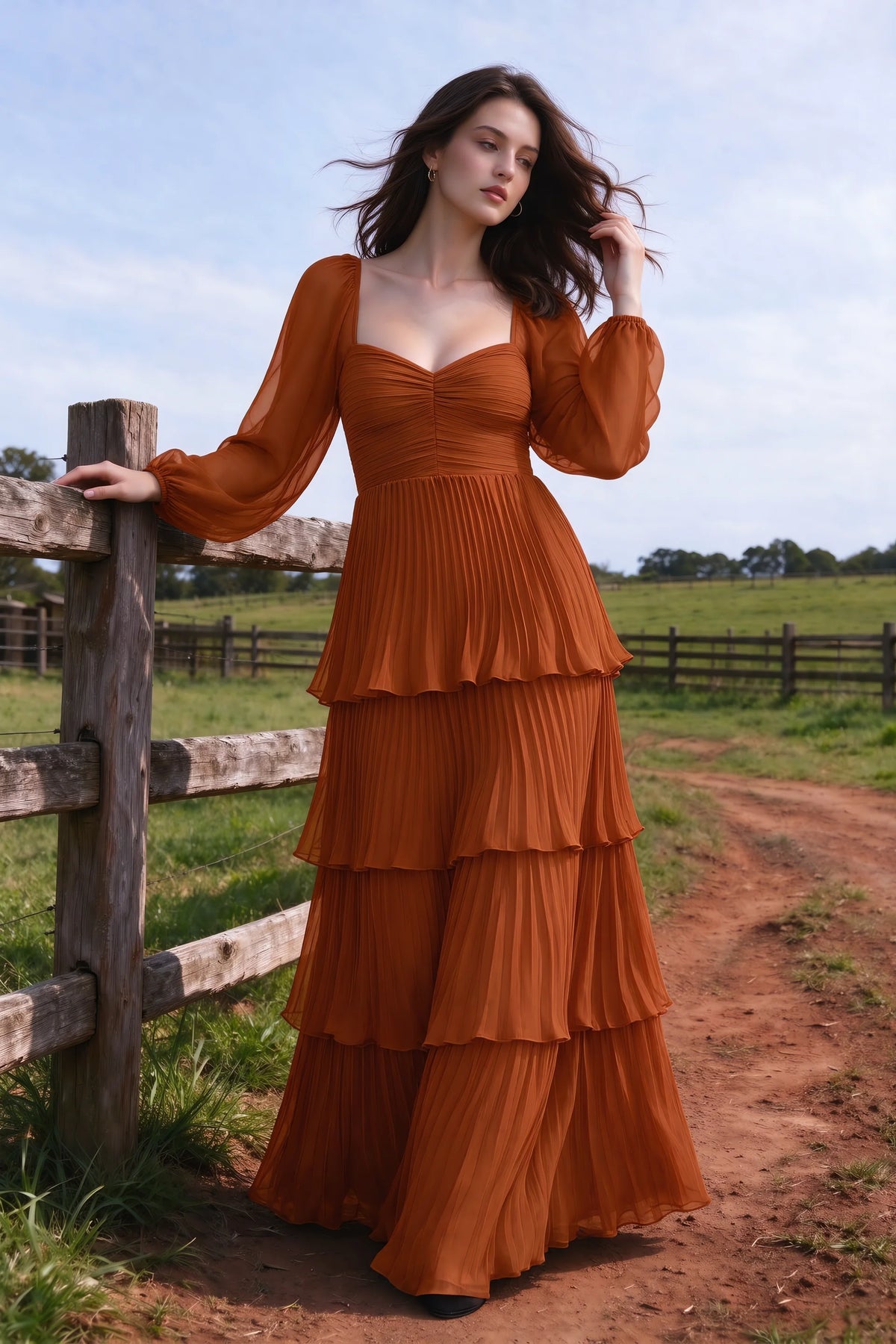 Outdoor front view by a countryside fence of Sienna rust tiered pleated maxi dress with a long flowing skirt
