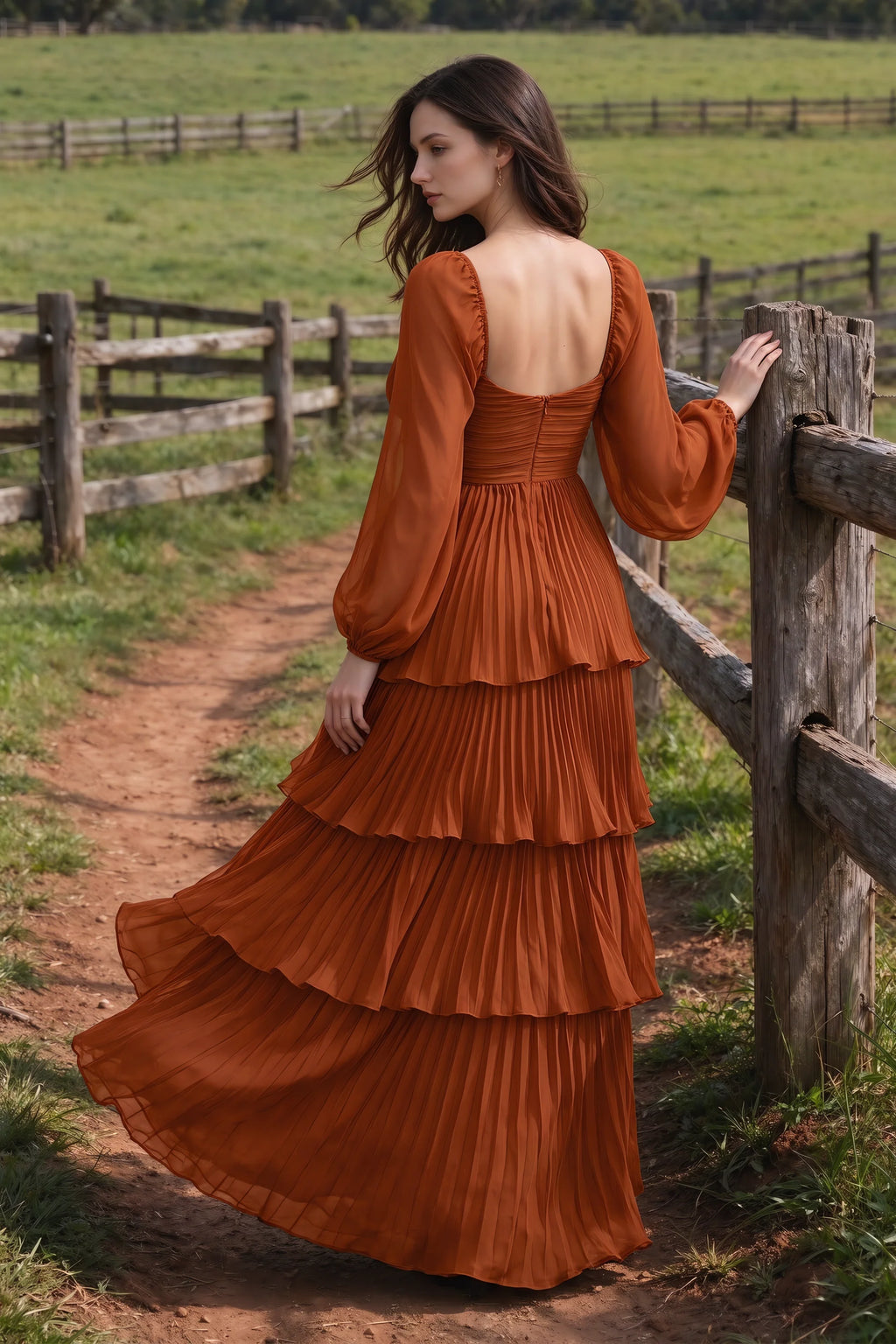 Outdoor rear view by a countryside fence of Sienna rust tiered pleated maxi dress with a long flowing skirt
