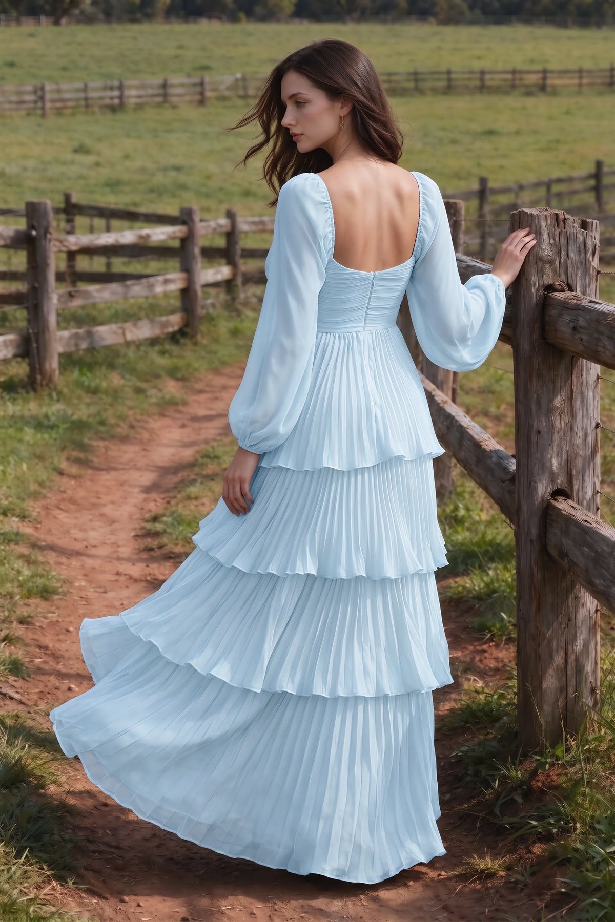 Outdoor rear view by a countryside fence of Sienna sky blue tiered pleated maxi dress with a long flowing skirt