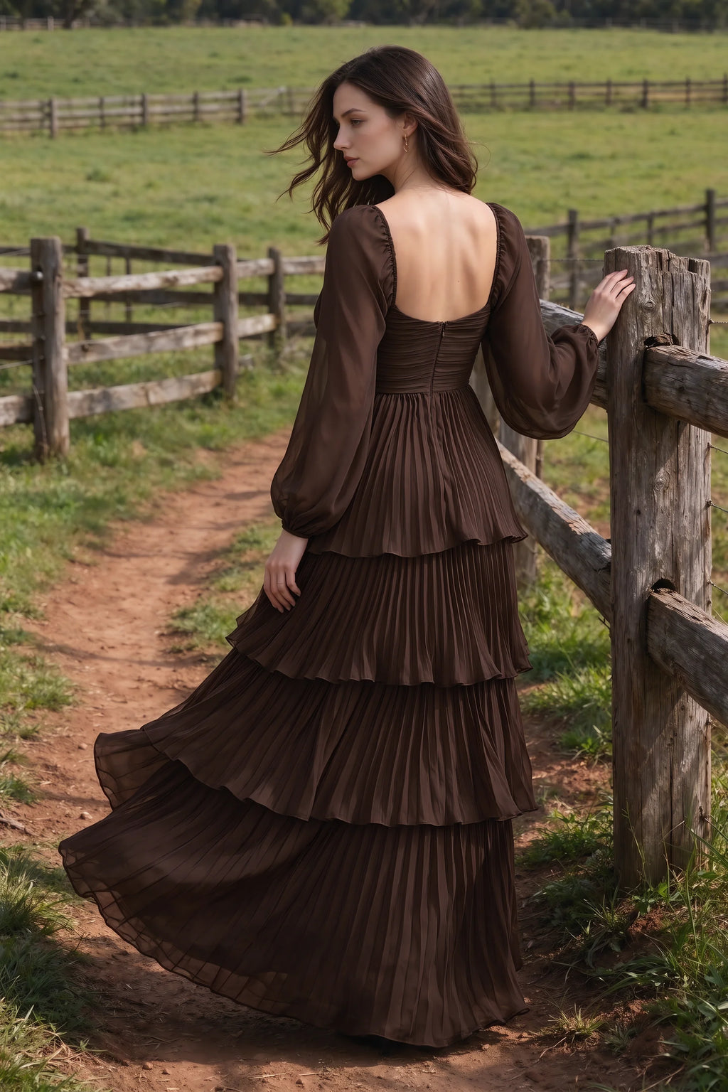 Outdoor rear view by a countryside fence of Sienna truffle tiered pleated maxi dress with a long flowing skirt
