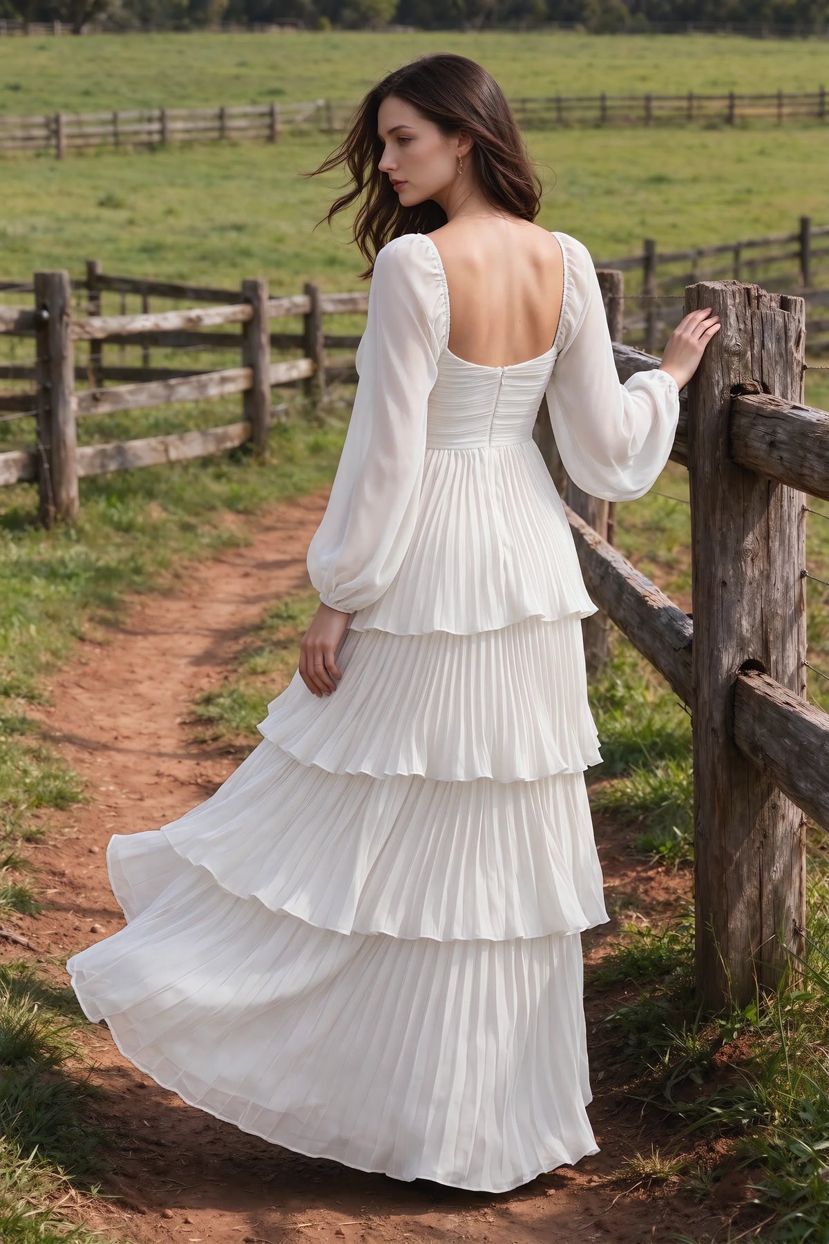 Outdoor rear view by a countryside fence of Sienna white tiered pleated maxi dress with a long flowing skirt
