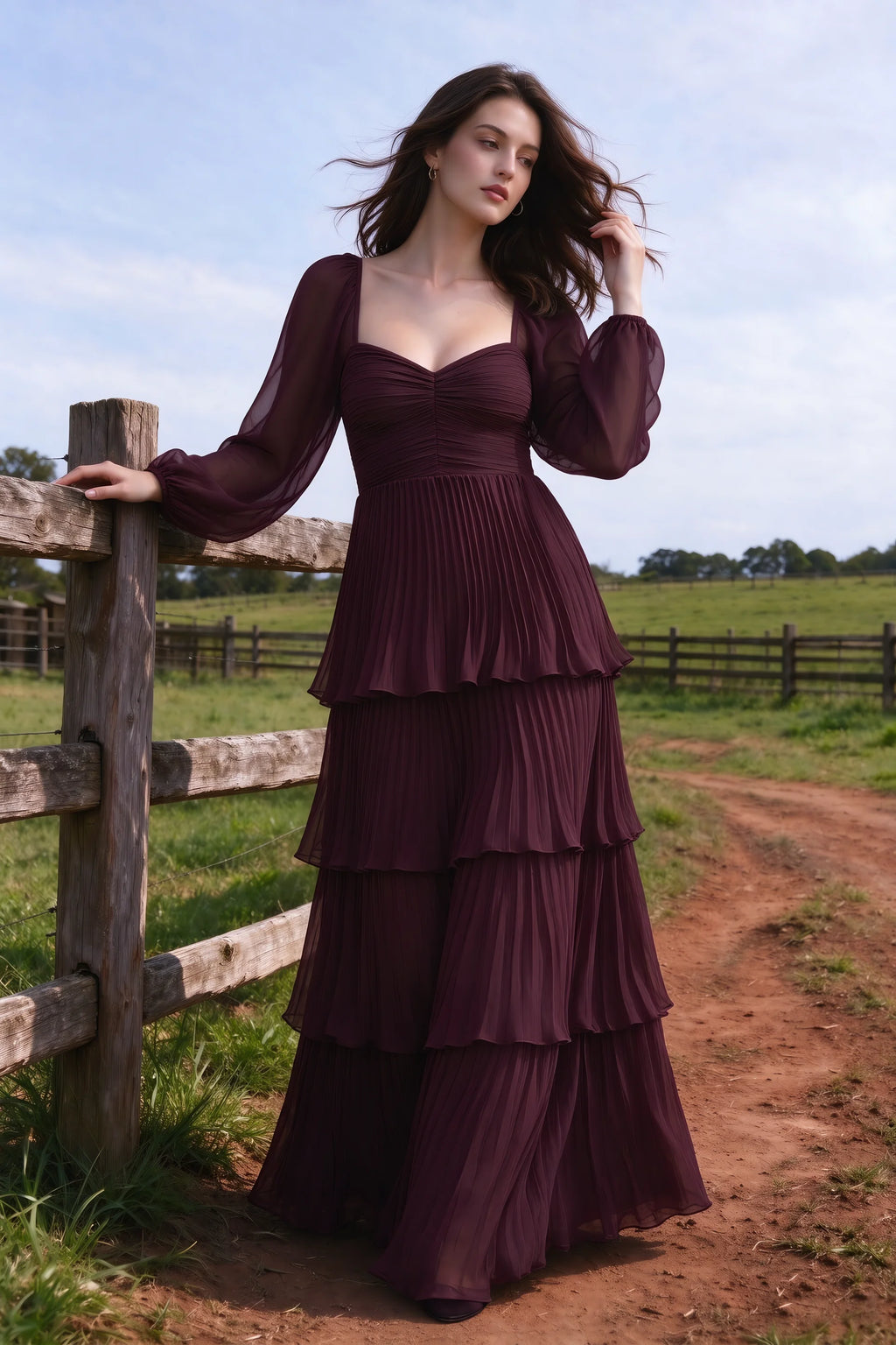 Outdoor front view by a countryside fence of Sienna wine tiered pleated maxi dress with a long flowing skirt