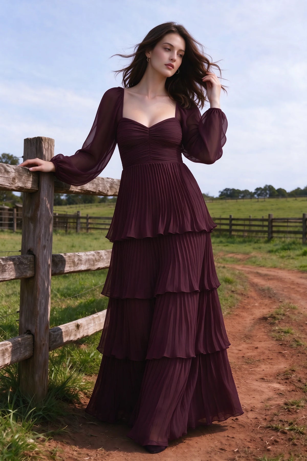 Outdoor front view by a countryside fence of Sienna wine tiered pleated maxi dress with a long flowing skirt