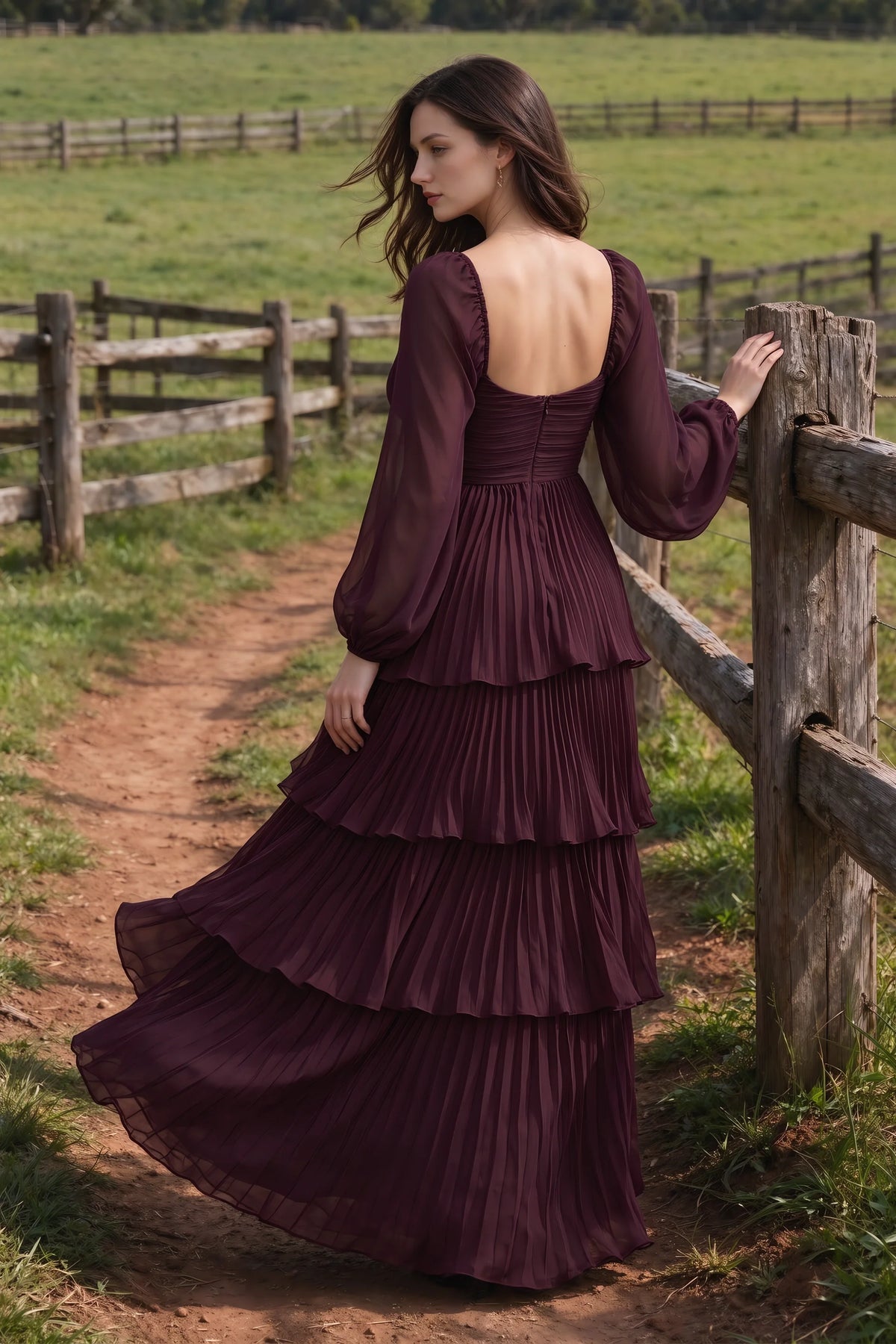 Outdoor rear view by a countryside fence of Sienna wine tiered pleated maxi dress with a long flowing skirt