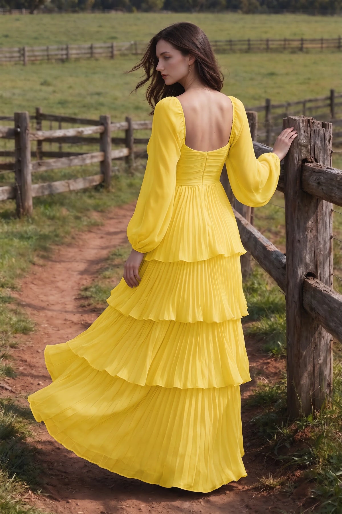 Outdoor rear view by a countryside fence of Sienna yellow tiered pleated maxi dress with a long flowing skirt